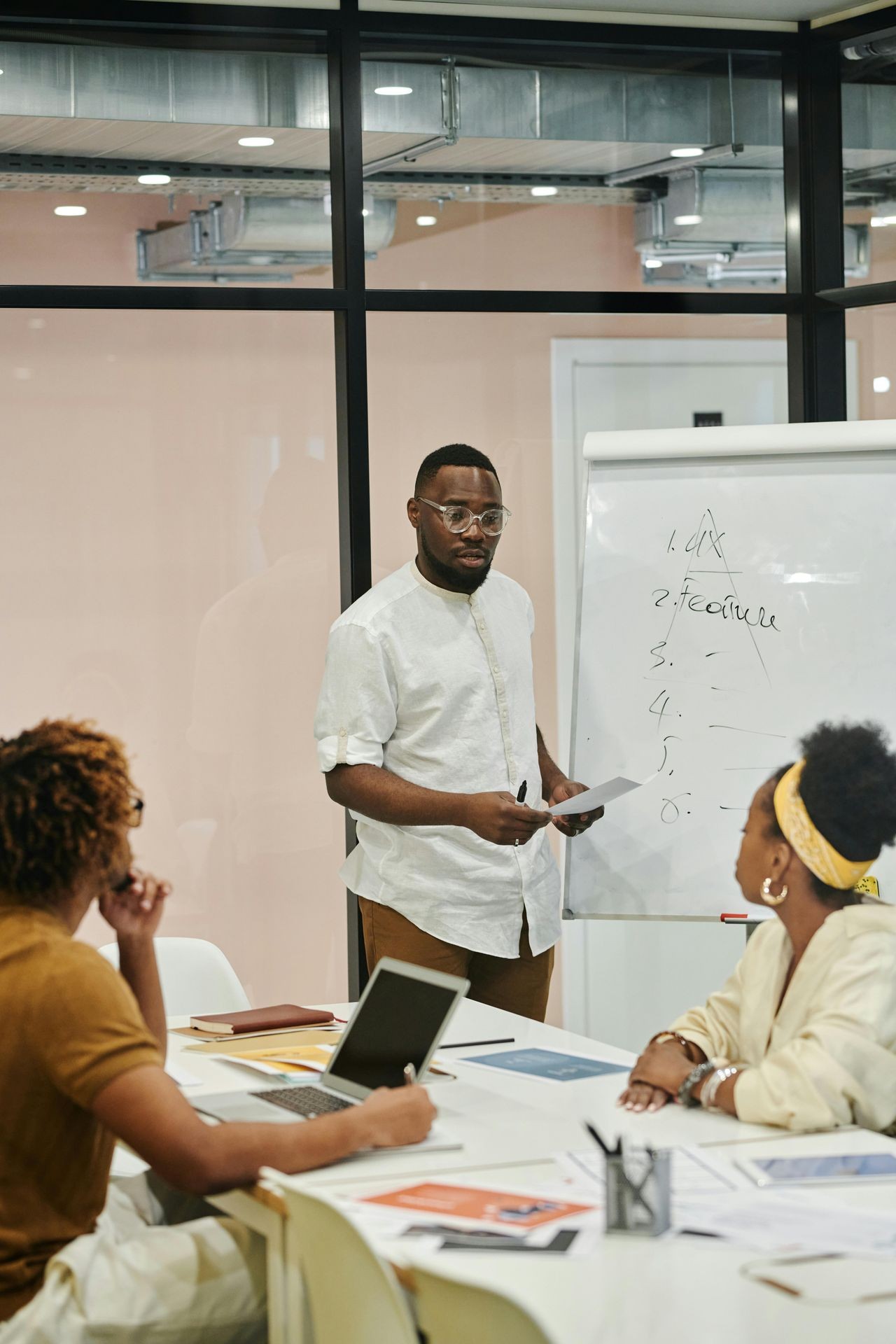 "Three business professionals engaged in a strategic planning session in a modern office. One team member presents key objectives on a whiteboard, while the others actively participate with laptops and documents, fostering collaboration, leadership, and business growth."