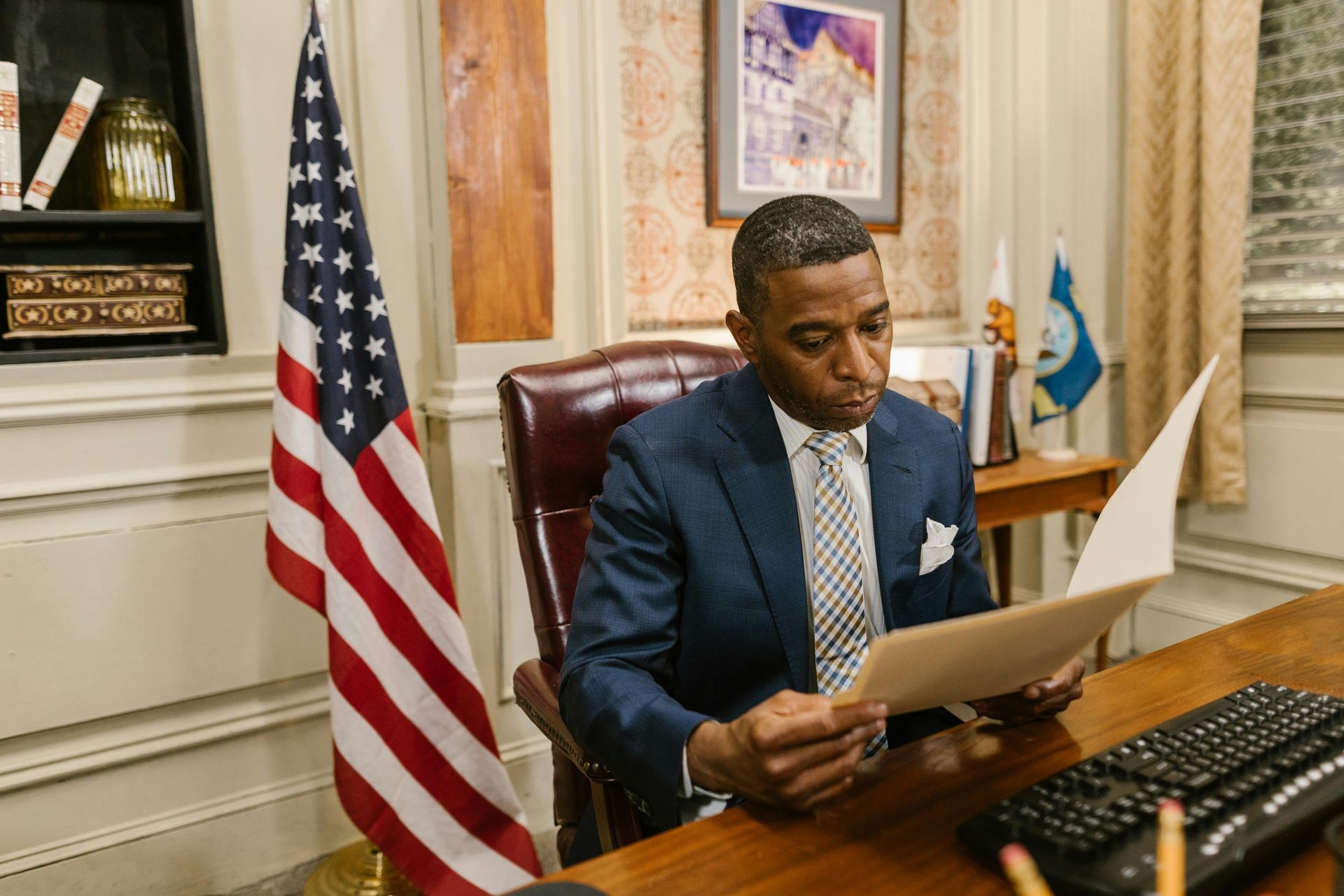 "Professional business consultant reviewing a government contract proposal at an executive office desk. The setting includes an American flag, legal documents, and a formal office environment, emphasizing expertise in government contract writing, business consulting, and proposal development. Ideal for businesses seeking federal contracts, grant funding, and strategic growth planning."