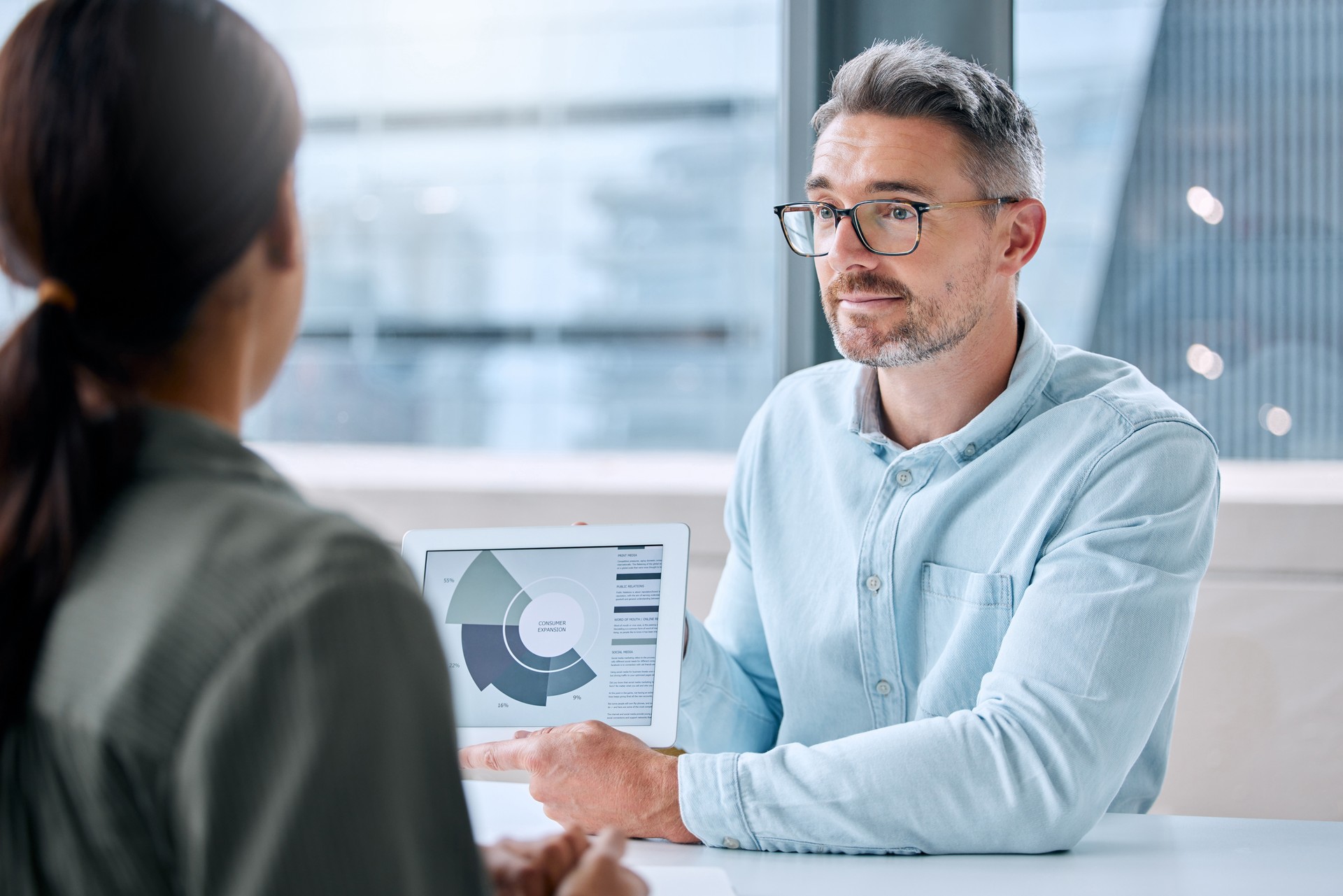 Shot of mature businessman researching potential grant-makers speaking to a colleague while analyzing graphs on a digital tablet in an office